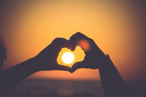 silhouette of person's hands forming heart in the evening sun