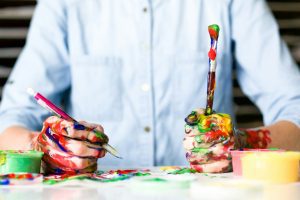 person holding click pen in one hand and a messy paintbrush in the other